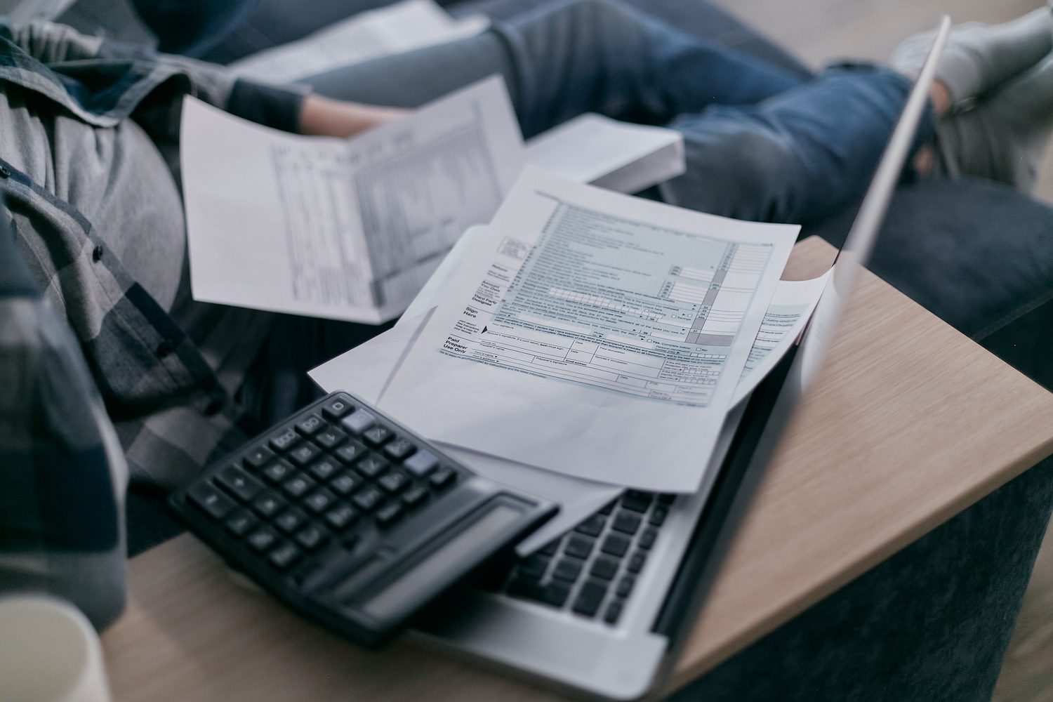 Someone at home in the evening, surrounded by paperwork with a calculator balanced on a laptop